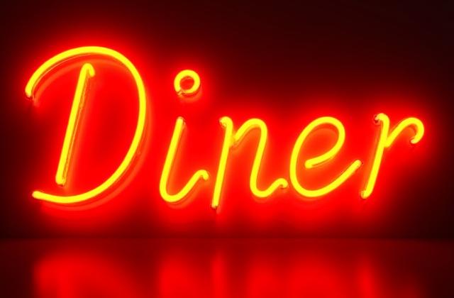 A close-up shot focusing on the rich red and yellow color and intricate detail of a hand-bent glass neon sign that reads 'Diner', with classic script font.