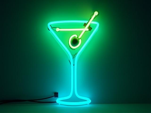 A retro neon sign shaped like a martini glass with an olive, glowing a brilliant green and blue.