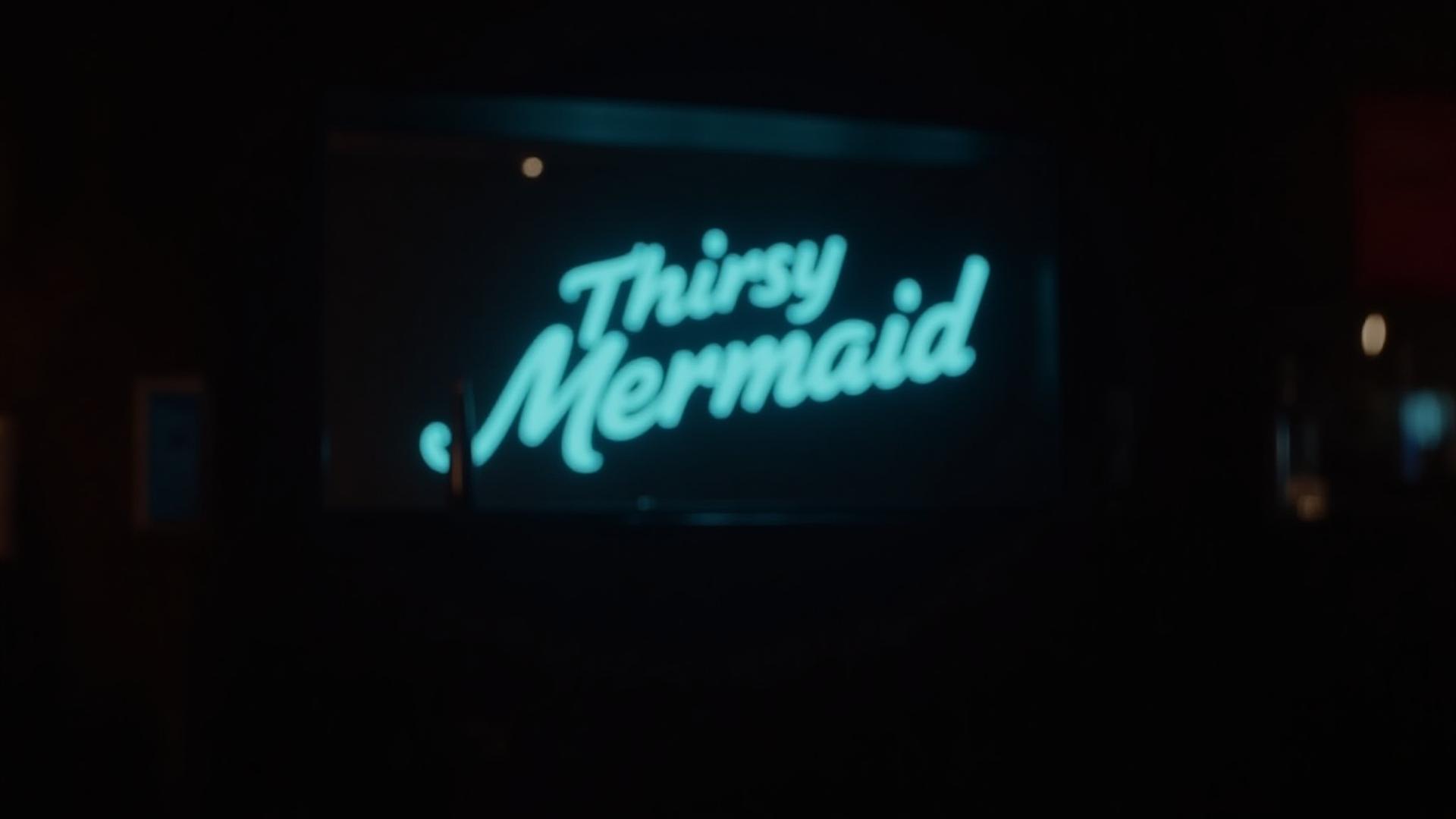 Interior of 'The Thirsty Mermaid' bar in Key West, dimly lit, with a prominent custom GALE D McNULTY neon sign glowing a soft blue behind the bar.
